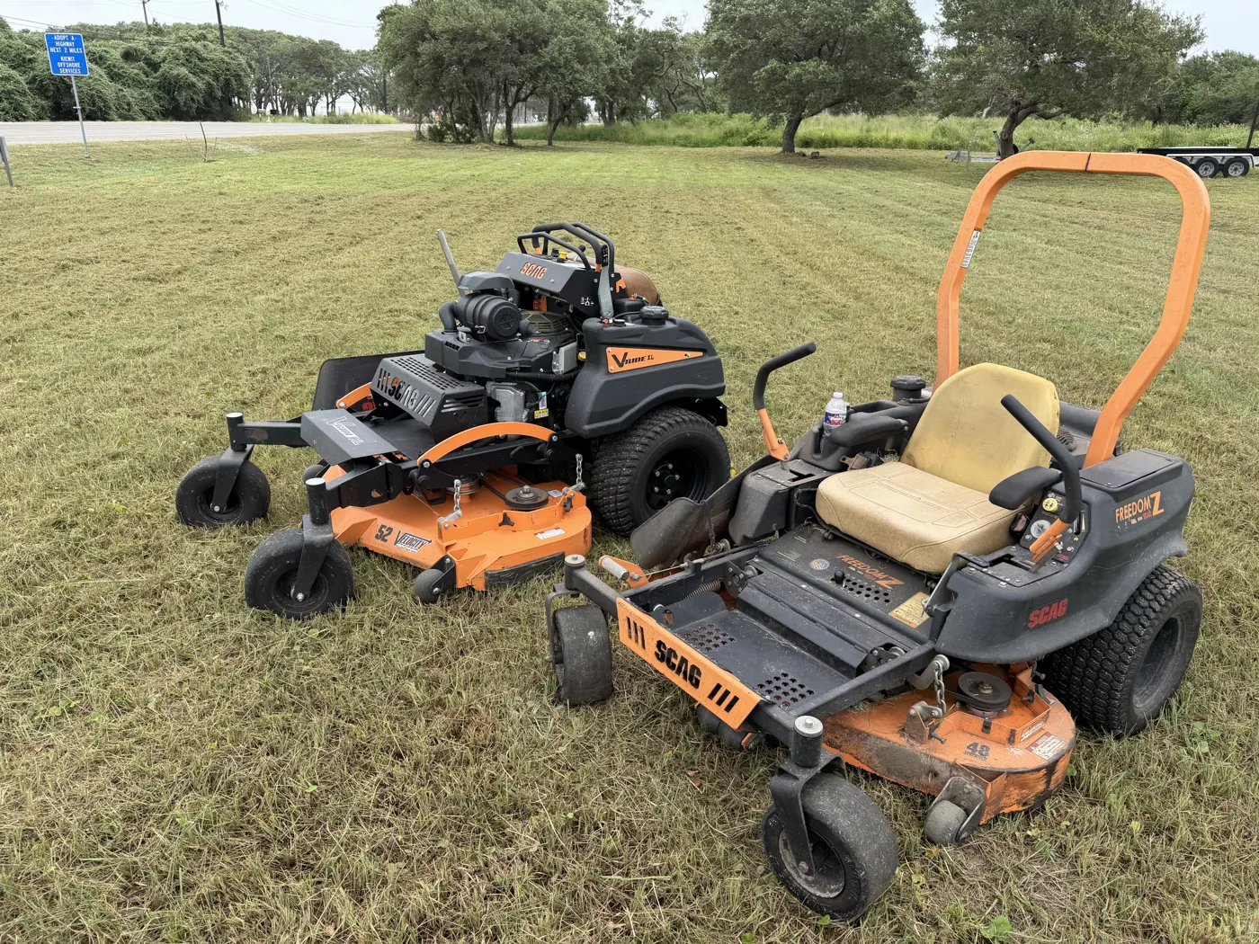 Two SCAG zero-turn mowers cutting a large open commercial field
