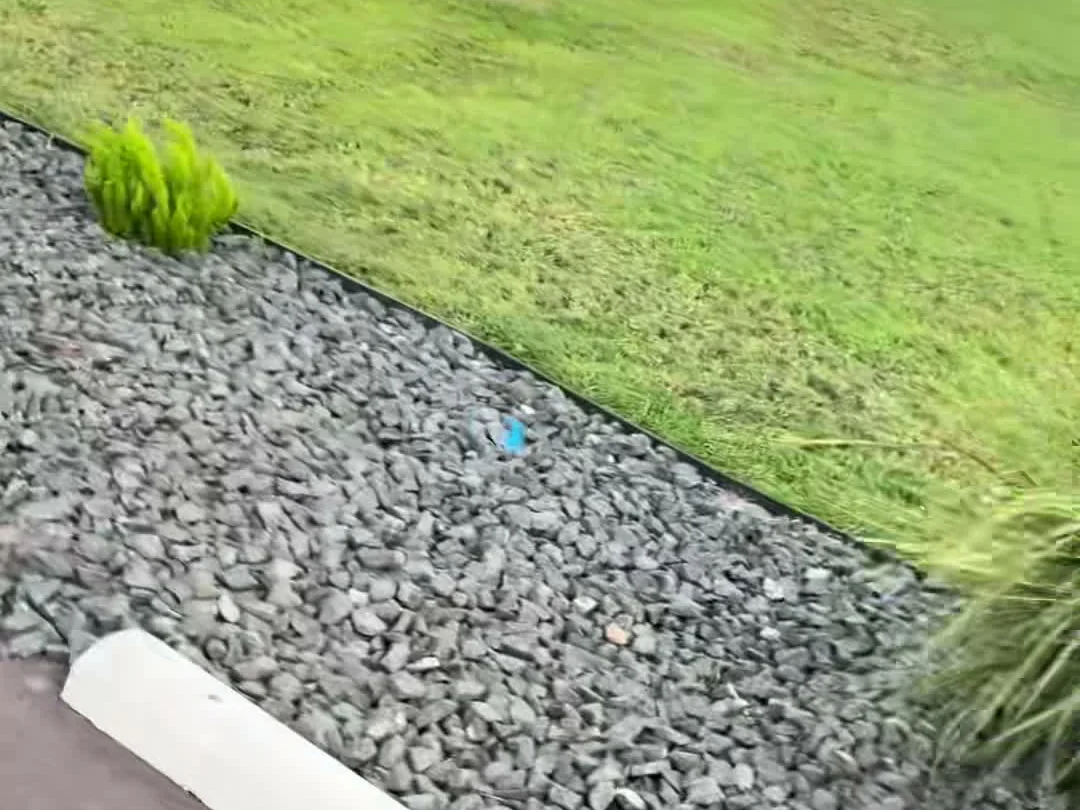 A fresh river-rock bed cut in along the mowed lawn at a commercial property