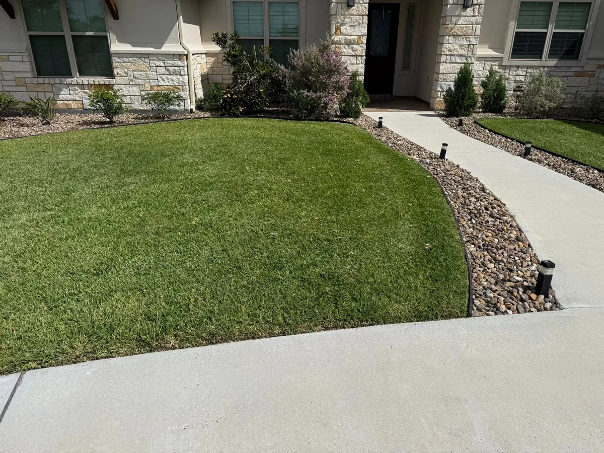 A freshly mowed front lawn with clean rock beds in front of a stone-fronted house